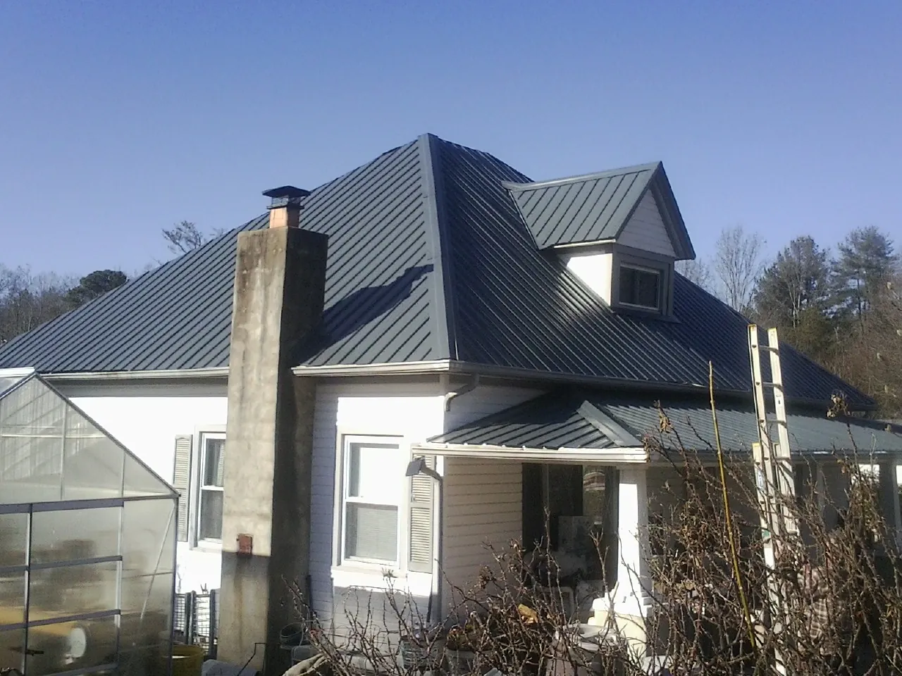 Dark blue standing seam metal roof on a white farmhouse with dormer — Slate & Tile Roof Repair by Roofing Brothers in Wardensville