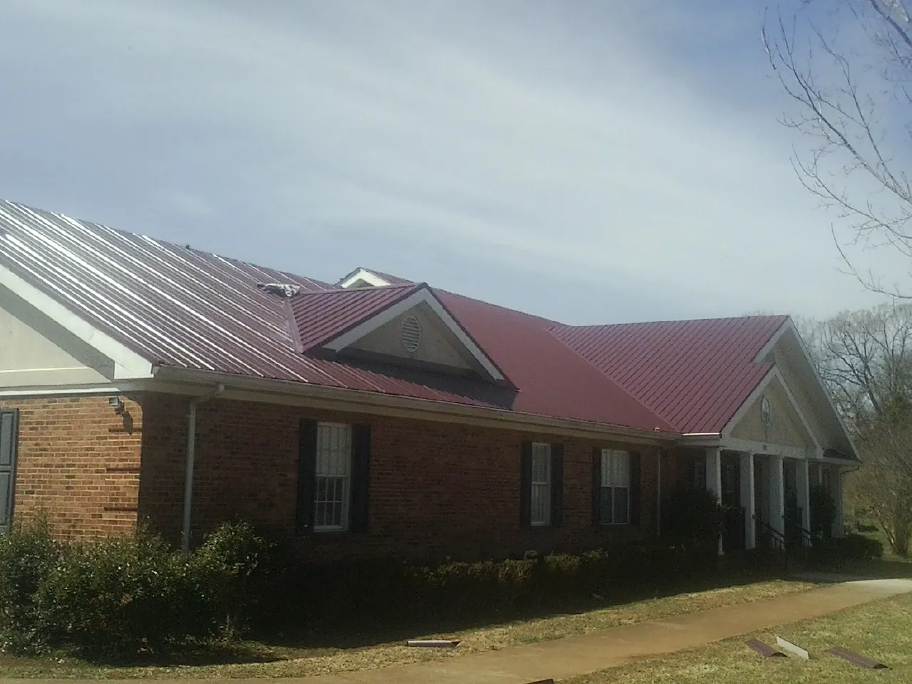Red metal roof with gabled entries on a long brick building, from a Hail Damage Roof Repair job in Wardensville