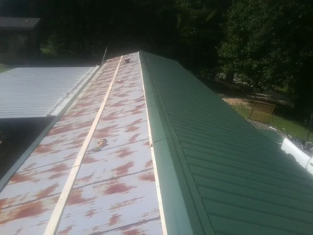 Old rusted panels beside newly installed green metal roofing — Wind Damage Roof Repair by Roofing Brothers in Wardensville
