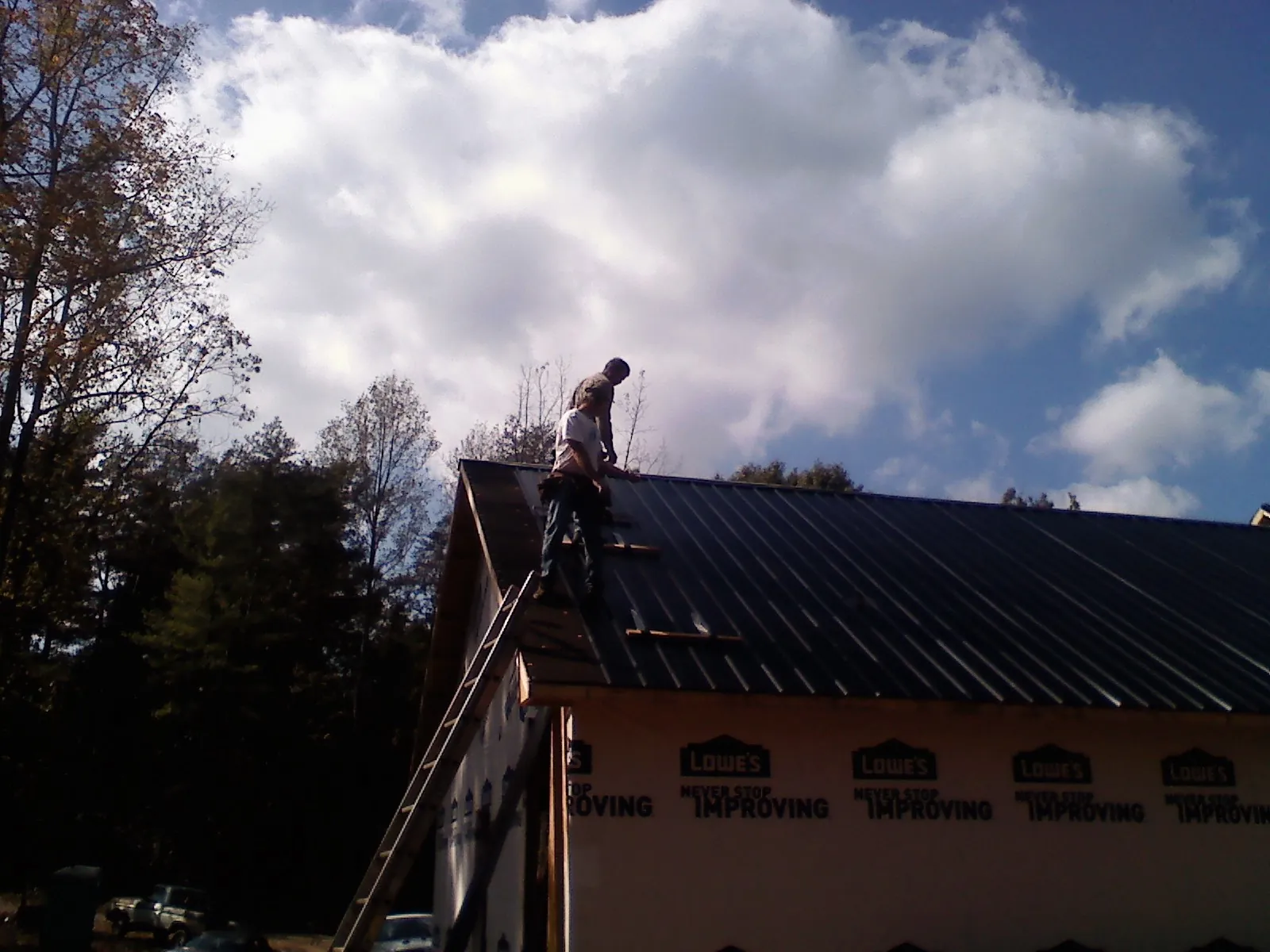 Roofer fastening dark metal panels high against a cloudy sky, from a Roof Inspection job in Wardensville