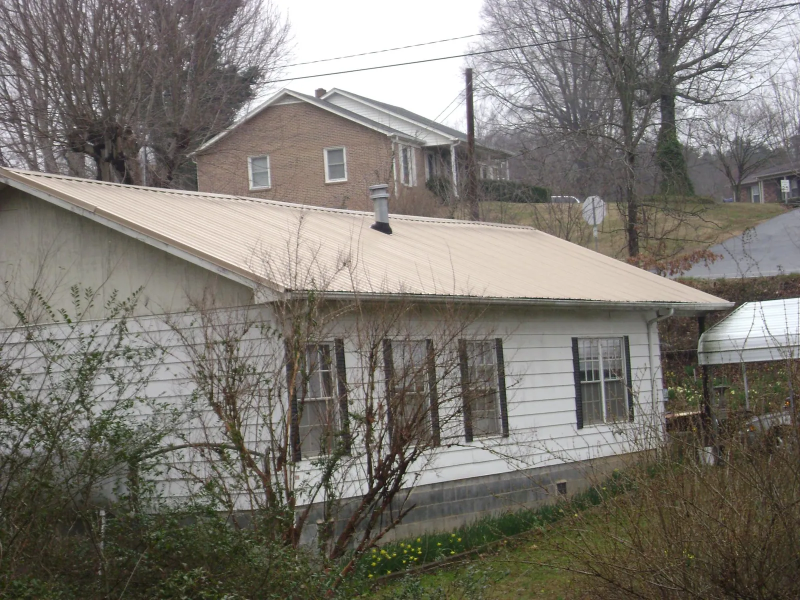 Tan metal roof on a white sided house set into a hillside — Commercial Roofing by Roofing Brothers in Wardensville
